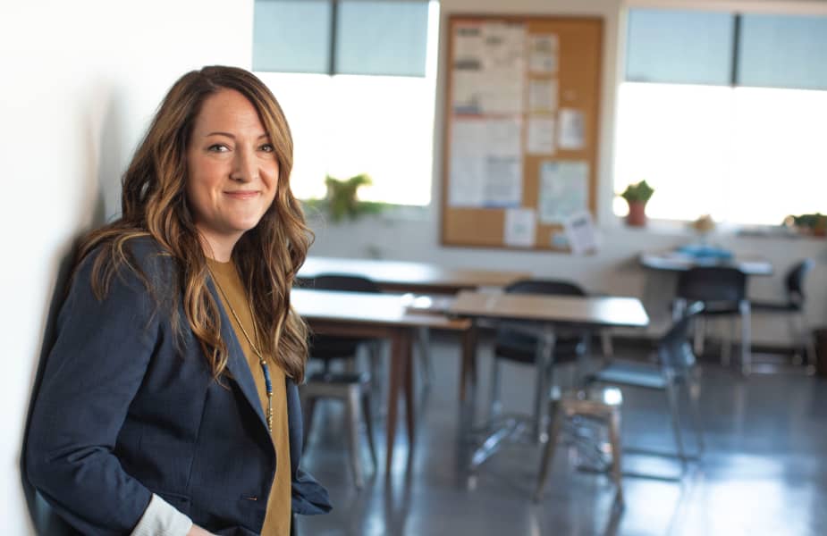 Teacher in her classroom leaning against a wall